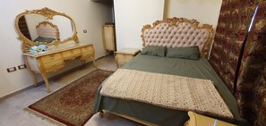 A bedroom with a bed, a vanity with a mirror, and a small table. - Charming sunset,with Panoramic Nile view and pyramid view. (Cairo)
