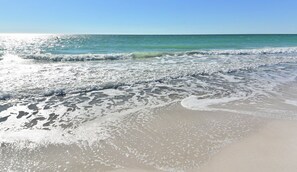 A beach with waves gently lapping onto the shore, clear skies, and a calm sea. - Beachside Duplex in Anna Maria – Steps to Gulf Beaches | FREE WIFI | 4BR   Parking for 4 (Anna Maria)