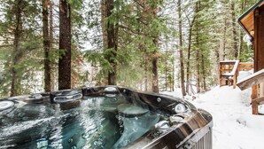 Un jacuzzi rodeado de altos árboles y una terraza de madera.