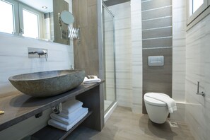 A modern bathroom with a large stone sink, a glass shower enclosure, and a toilet with a towel on it.