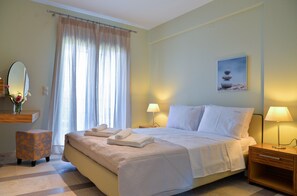 A neatly made bed with white linens, a bedside table with a lamp, a small stool, and a framed picture on the wall. - Drimonari Villas (Lefkada)