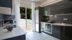 A modern kitchen with dark cabinets, a built-in oven, and a large window. - Drimonari Villas (Lefkada)
