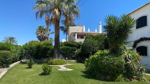 Un giardino curato con palme e un vialetto lastricato che conduce a un edificio con facciata bianca e una torre.