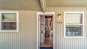 A wooden exterior with a door leading to a kitchen and living area, a number '100' on the wall, and a welcome mat. - Bluebird View | Sierra Blanca Views + Hot Tub Retreat (Ruidoso)