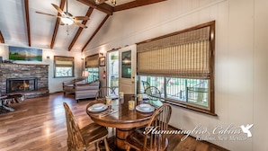 A spacious dining area with a wooden table and chairs, a fireplace, and large windows with blinds. - Bluebird View | Sierra Blanca Views + Hot Tub Retreat (Ruidoso)