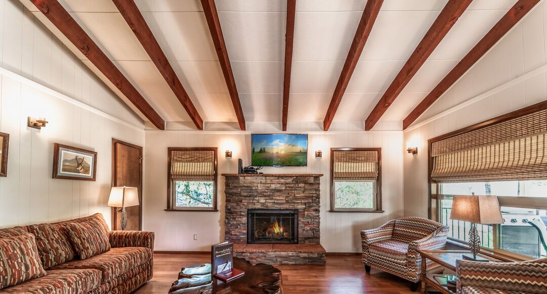 A spacious living room with a stone fireplace, wooden beams, and patterned furniture.