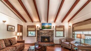 A spacious living room with a stone fireplace, wooden beams, and patterned furniture.