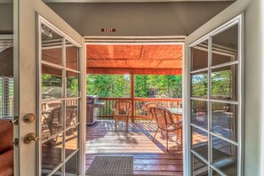 Puerta abierta que da a una terraza techada con una parrilla, sillas y vistas a árboles.