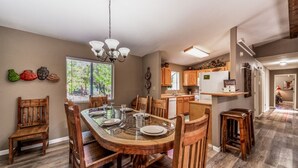 Un vaste espace dédié à la salle à manger, avec une grande table et des chaises en bois, un lustre, et une vue sur la cuisine en arrière-plan.