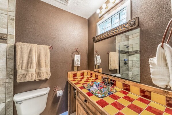 A bathroom with a checkered tile floor, a white toilet, and a mirror with lights above it.