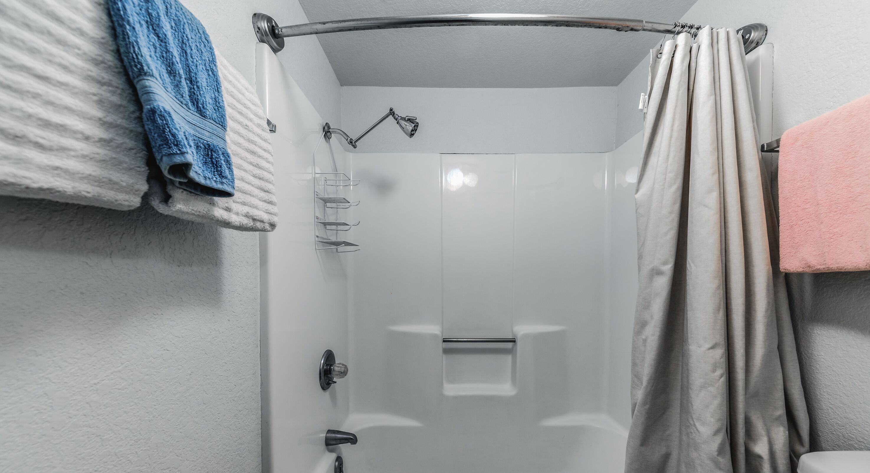 A shower with a glass door, a towel rack with a blue towel, and a beige curtain.