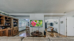 Una sala de estar con una estantería de madera, una mesa redonda de centro y un televisor que muestra una imagen floral.