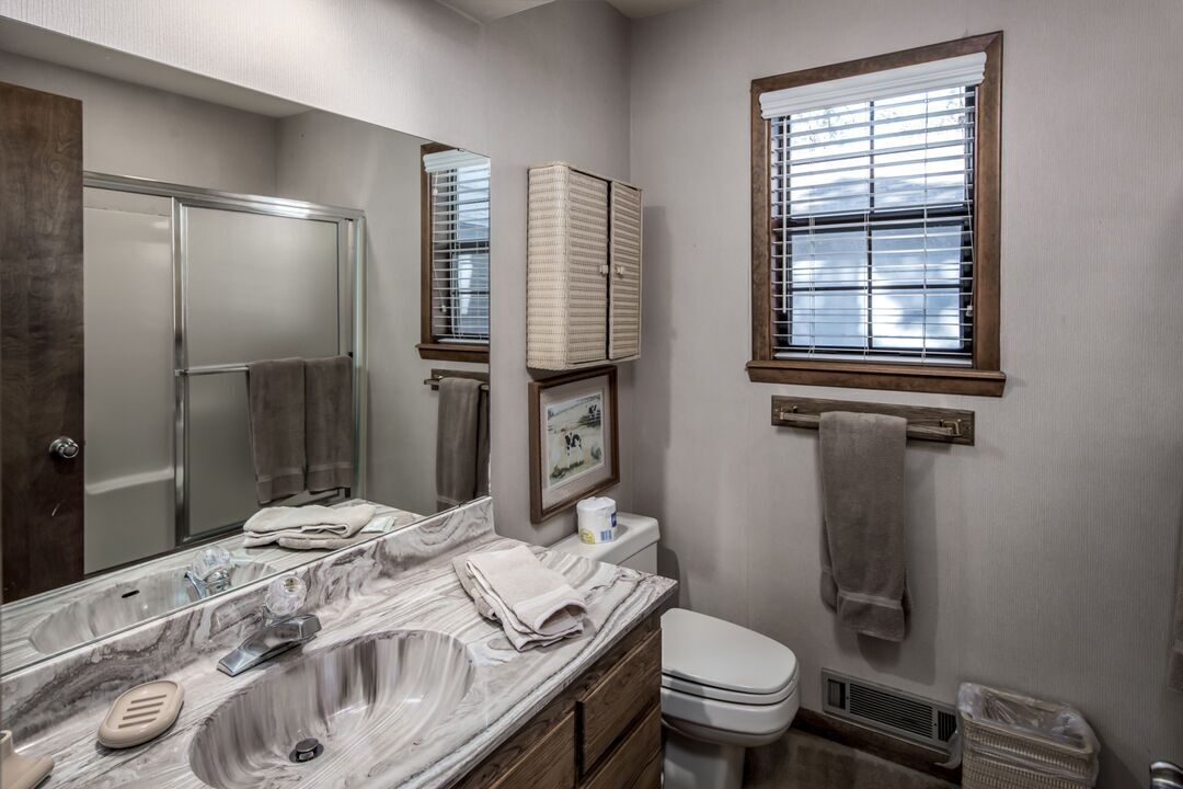 A bathroom with a marble sink, a toilet, a window with blinds, and a mirror.
