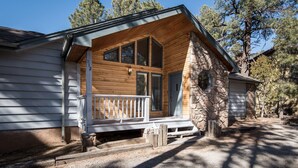 A cabin with a stone exterior, a wooden porch, and a large window. - Angulo | Your Perfect Angle on Relaxation w/ Hot Tub & Deck (Alto)