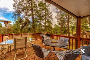 Un patio extérieur abrité, équipé d’un barbecue, de sièges et offrant une vue sur une forêt.