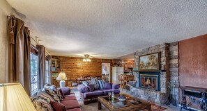 Un intérieur de chalet chaleureux avec une cheminée en pierre, des murs en bois et un coin salon confortable.