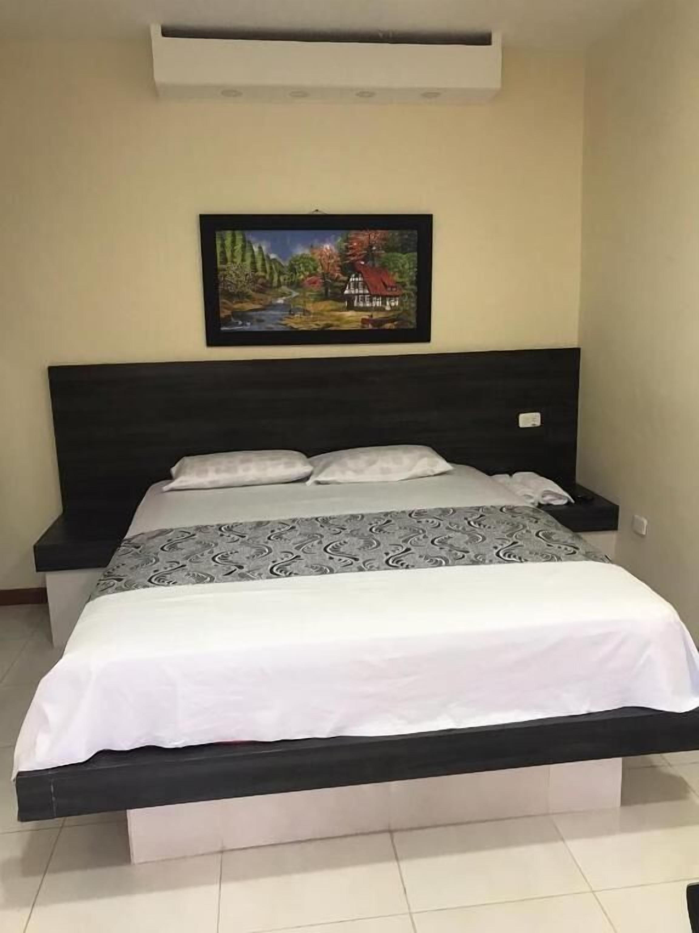 A bedroom with a bed, a nightstand, and a painting on the wall.