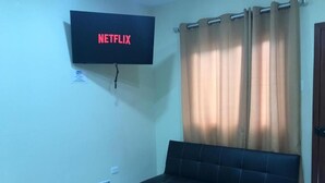 A living room with a black sofa, a glass coffee table, and a flat-screen TV mounted on the wall displaying the Netflix logo. - Hostería Pacific Stone (Tachina)