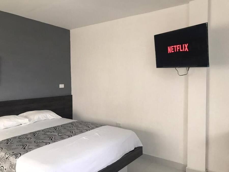 A hotel room with a bed, a wall-mounted TV displaying "NETFLIX," and a plain wall.