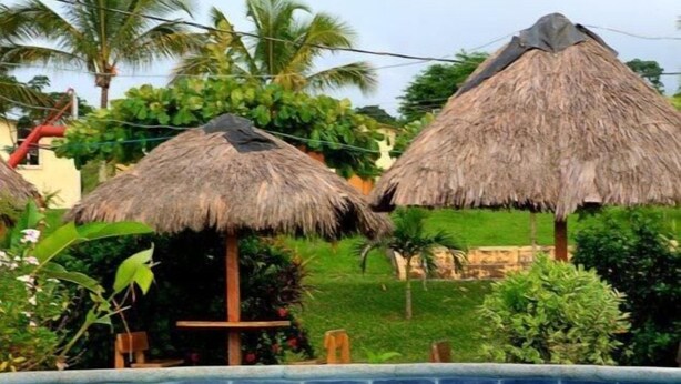 A swimming pool with thatched umbrellas and lush greenery in the background. - Hostería Pacific Stone (Tachina)