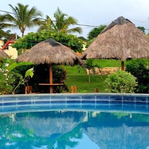 A swimming pool with thatched umbrellas and lush greenery in the background. - Hostería Pacific Stone (Tachina)
