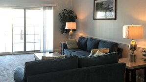 Ett vardagsrum med en mörkblå soffa, ett soffbord, en lampa och en takfläkt. Det finns ett stort fönster med utsikt.