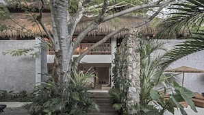 A wooden pathway flanked by tropical plants leading to a building with a thatched roof and a balcony. - Casa Hormiga (Bacalar)