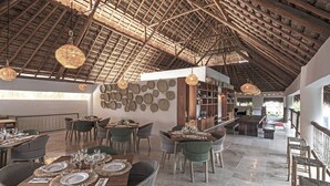 A spacious dining area with high ceilings and natural light, featuring wooden tables and chairs, a variety of hanging lights, and a wall adorned with circular decorations. - Casa Hormiga (Bacalar)