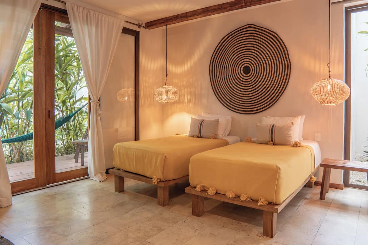 Une chambre avec deux lits, un grand élément de décoration circulaire au mur et un hamac à l’extérieur.