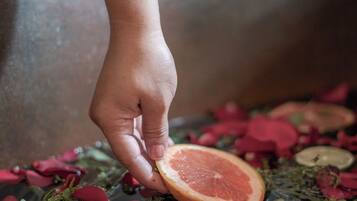 Una mano recogiendo pomelo de un lecho de pétalos de rosa y rodajas de cítricos.