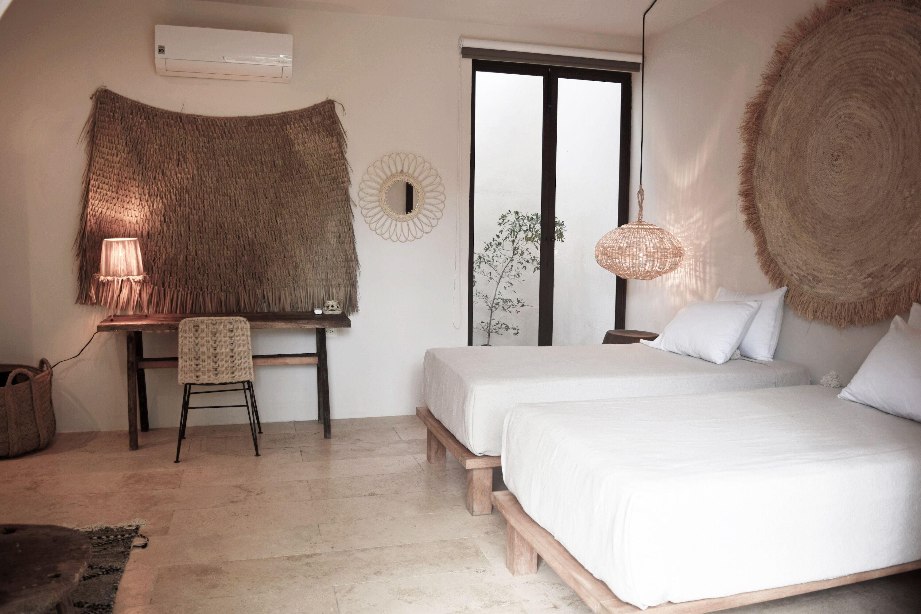 A bedroom with two beds, a desk with a chair, a hanging lamp, and a large woven tapestry on the wall.