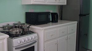 Una cucina con mobili bianchi, un fornello, un forno a microonde e un frigorifero.