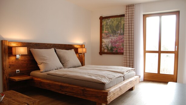 Een houten bed met hoofdeinde, twee nachtkastjes en een groot raam met gordijnen.
