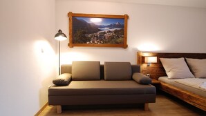 Een gezellige kamer met een sofa, een bed, een houten hoofdbord, een aan de muur hangend schilderij en een vloerlamp.