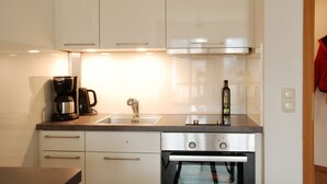 Een moderne keuken met witte kastjes, een roestvrijstalen oven, een koffiezetapparaat en een fles op het aanrecht.