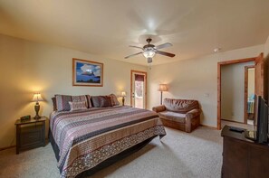 A bedroom with a bed, a chair, a ceiling fan, a nightstand, a lamp, a framed picture, and a door.