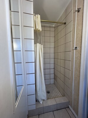 Ein kleiner Duschbereich mit gefliestem Boden, einem weißen Duschvorhang und einer Metallstange.