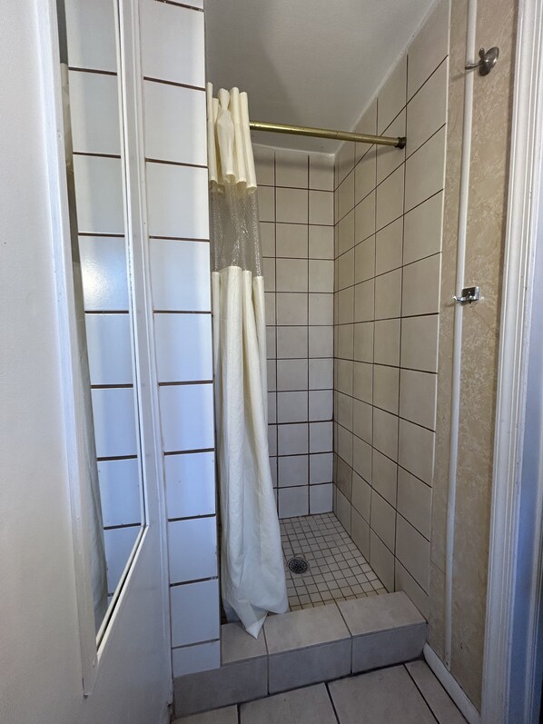 Pequeño espacio de ducha con azulejos, cortina blanca y barra de metal.