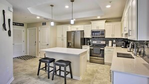 A modern kitchen with white cabinets, stainless steel appliances, and a central island with stools. - Kissimmee Condo w/ Resort-Style Amenities! (Kissimmee)