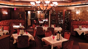 Un restaurante con mesas redondas, asientos tapizados en rojo y un candelabro.