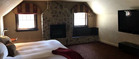 A bedroom with a bed, a ceiling fan, a fireplace, and a television.