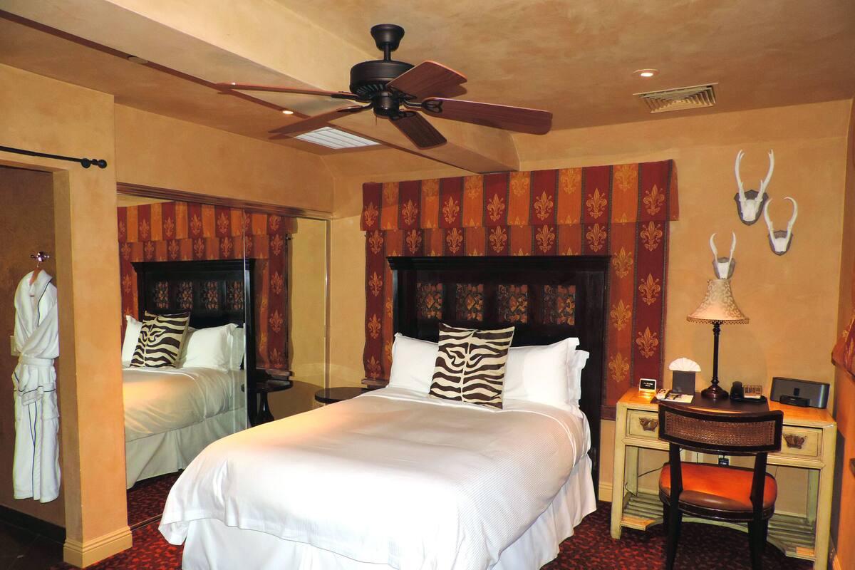 Habitación de hotel con una cama grande, ventilador de techo, mesita de noche con lámpara y un espejo.