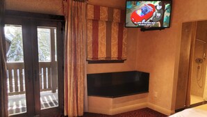 Habitación de hotel con un ventanal grande, una puerta corredera, una bañera y un televisor montado en la pared.