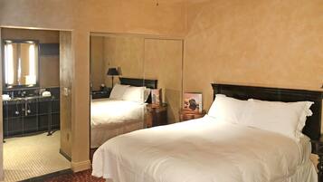 A hotel room with a large bed, a mirror, a nightstand, and a bathroom with a sink and mirror.