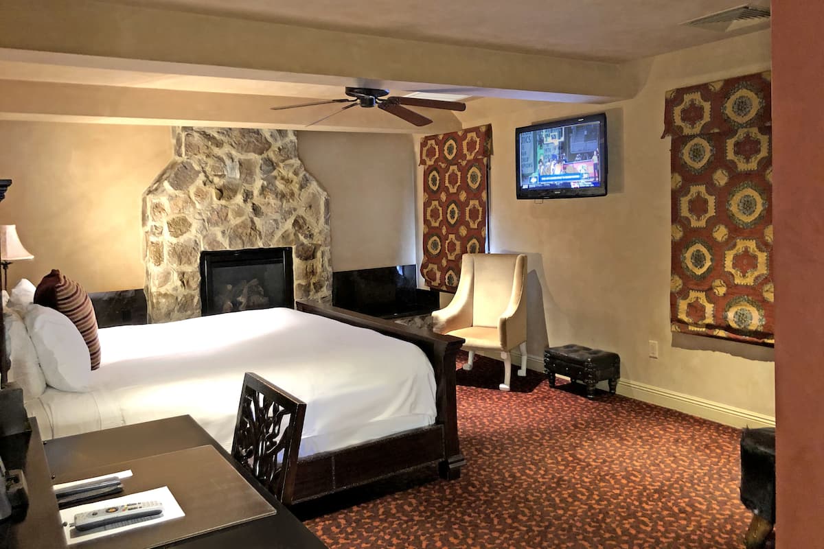 Habitación de hotel con chimenea de piedra, una cama, un televisor, un escritorio con silla y una alfombra estampada.