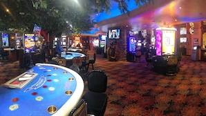 Zona de casino con máquinas tragamonedas, mesas de blackjack y piso alfombrado.