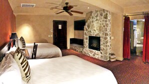 Habitación de hotel con dos camas, chimenea de piedra, ventilador de techo y televisión.