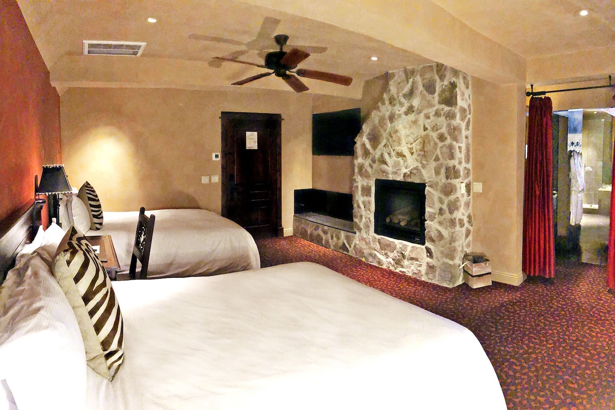 Habitación de hotel con dos camas, chimenea de piedra, ventilador de techo y televisión.