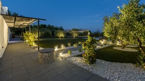 Un espace patio agrémenté d’une pergola, de bancs en pierre et d’un jardin bien éclairé, avec des arbres et une pelouse.