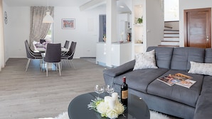 Un salon moderne avec un canapé gris, un coin repas comprenant une table et des chaises, et un escalier menant à un niveau supérieur.